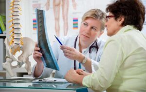 A chiropractor demonstrating a gentle back adjustment to a middle-aged patient in a health clinic setting.